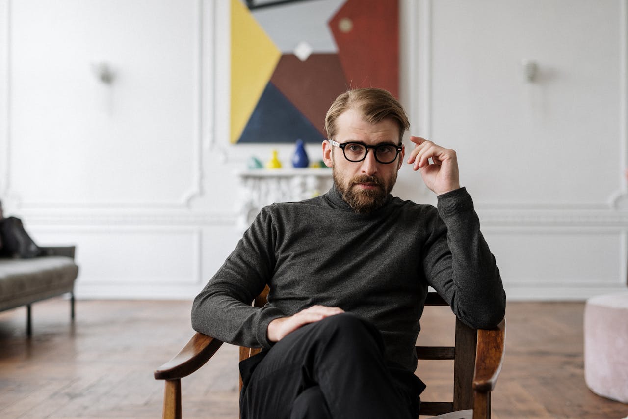 about-01 Man with glasses seated in modern interior with abstract art.