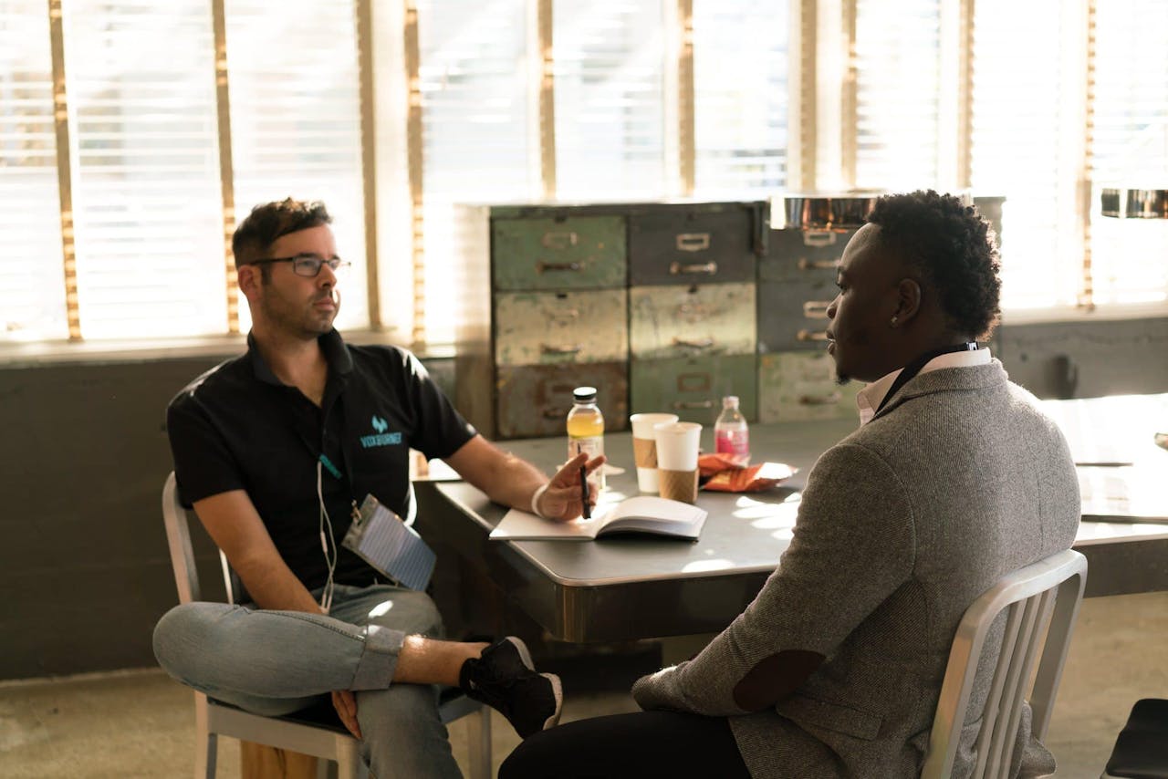 our-services-2 Two men having a focused business discussion in a sunlit office space.